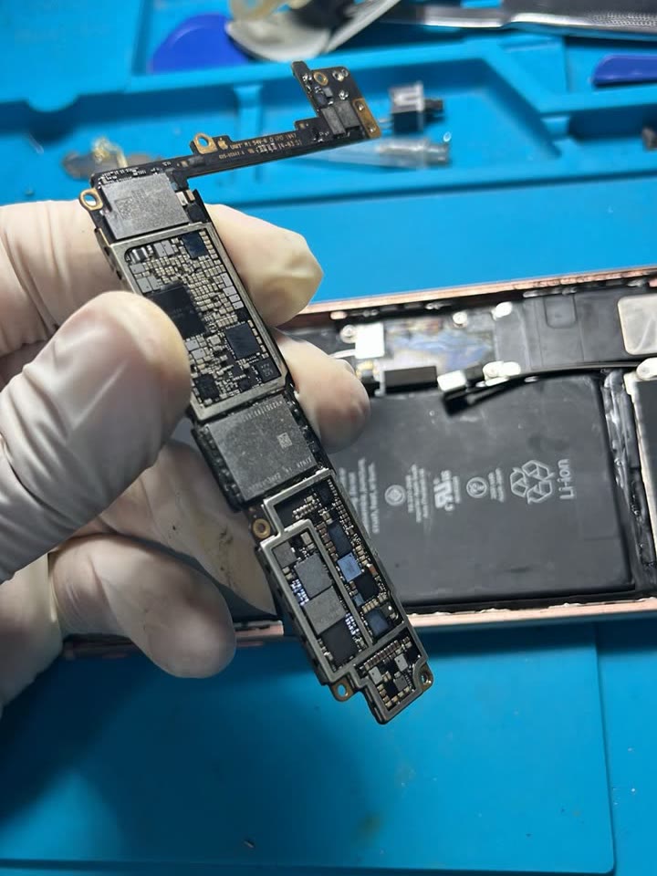 Mão com luva segurando a placa de um iPhone sobre tapete azul de bancada.